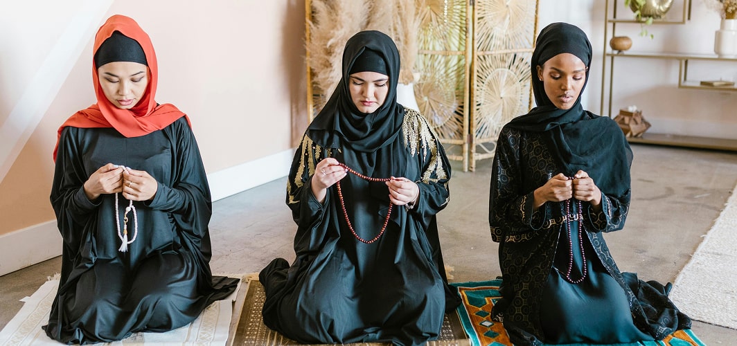 Three Muslim women kneeling on prayer mats with prayer beads